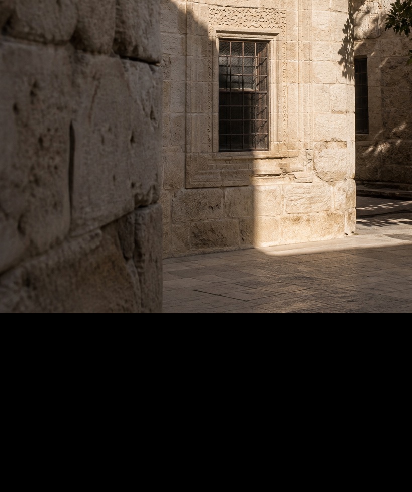 Stone courtyard passage with a grated window and a sharp band of daylight