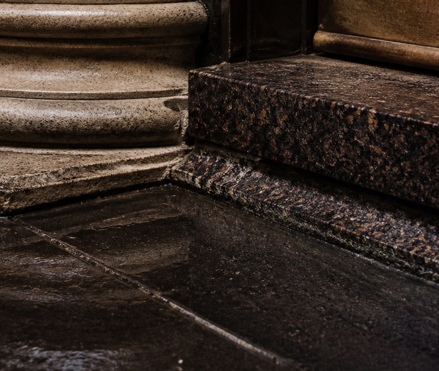 Stone column base meeting a polished granite step and a dark metal frame